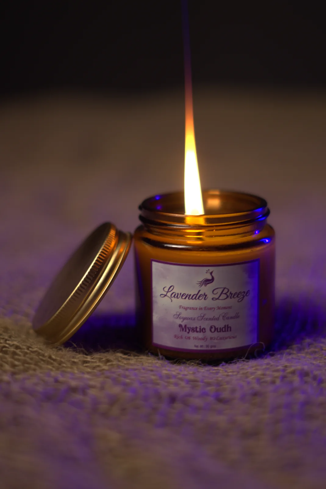 A lit Lavender Breeze soy candle in an amber glass jar, its lid set beside it