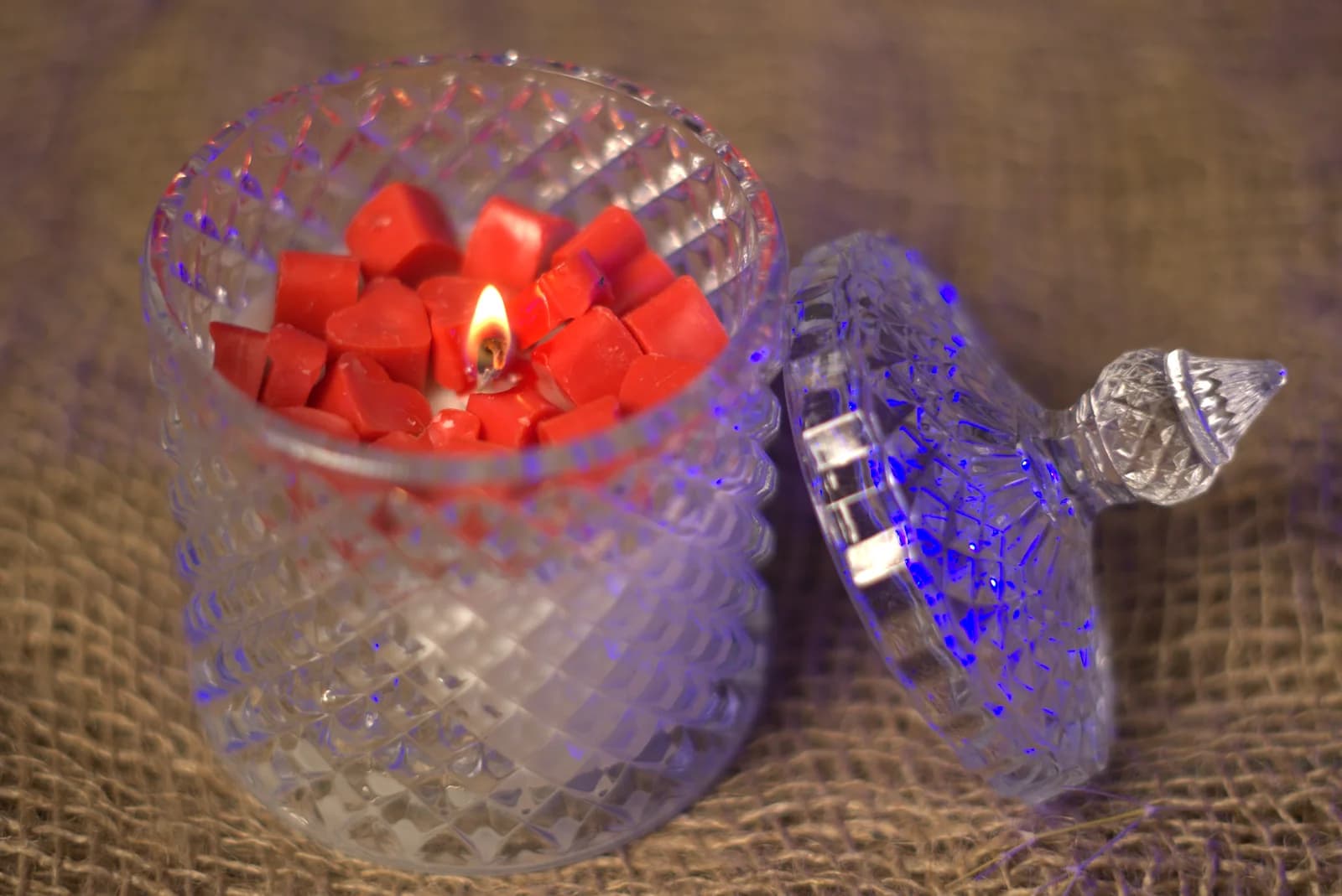 Lit soy wax candle in a cut-glass jar on hessian
